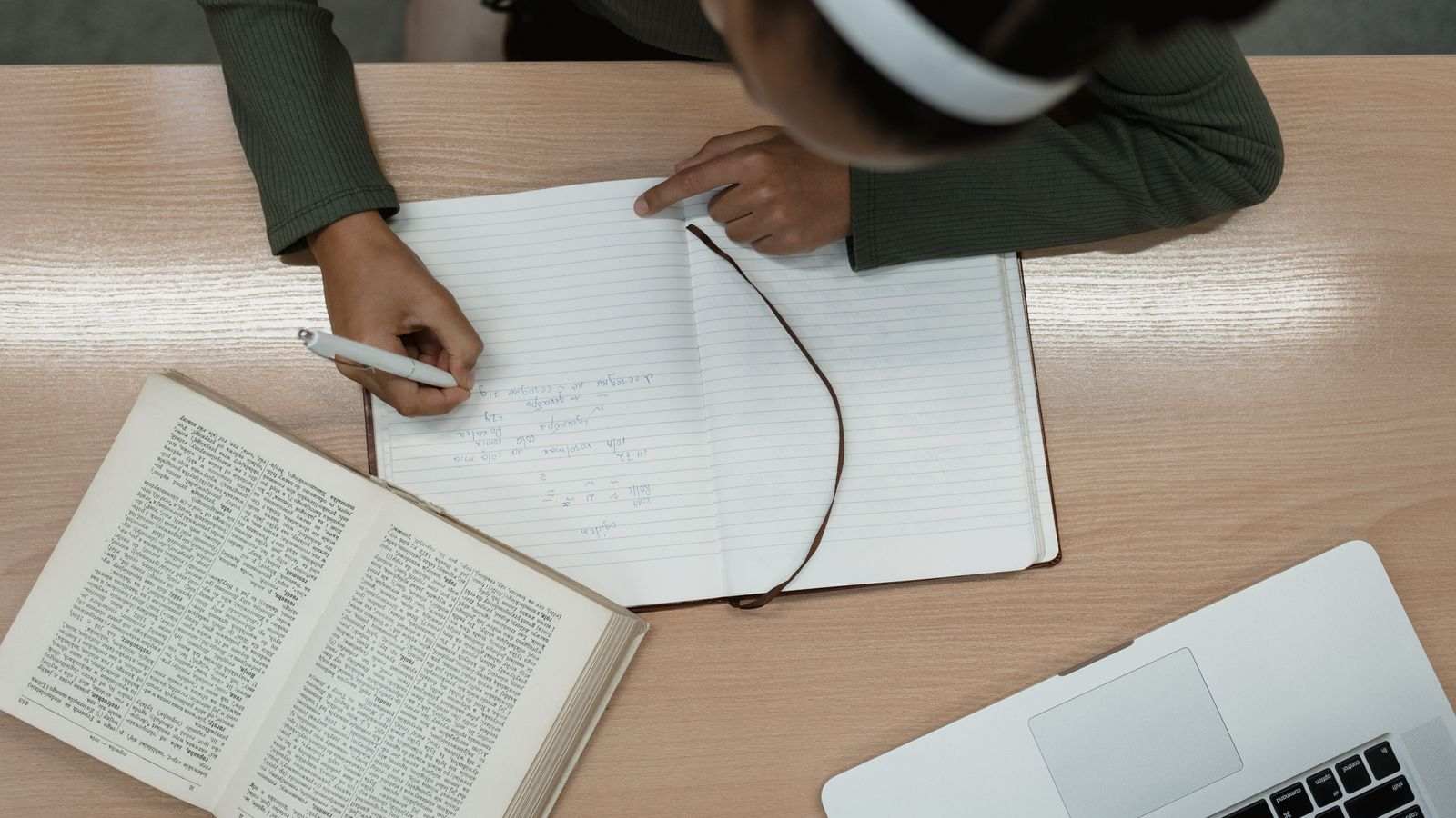 Vue du dessus d'une personne qui prend des notes près d'un livre ouvert et d'un ordinateur.