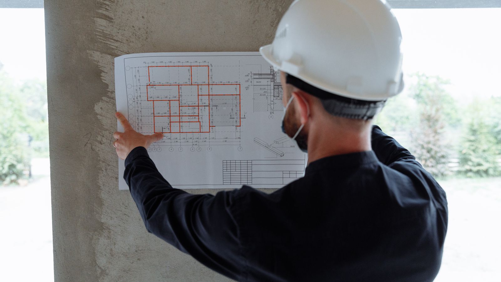 Vu de dos, un homme casqué consulte un plan d'étage fixé à un pilier de béton