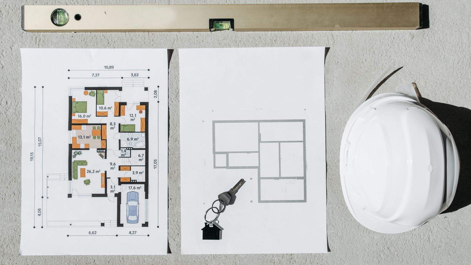 House floor plans, a spirit level and a white hard hat laid flat on concrete
