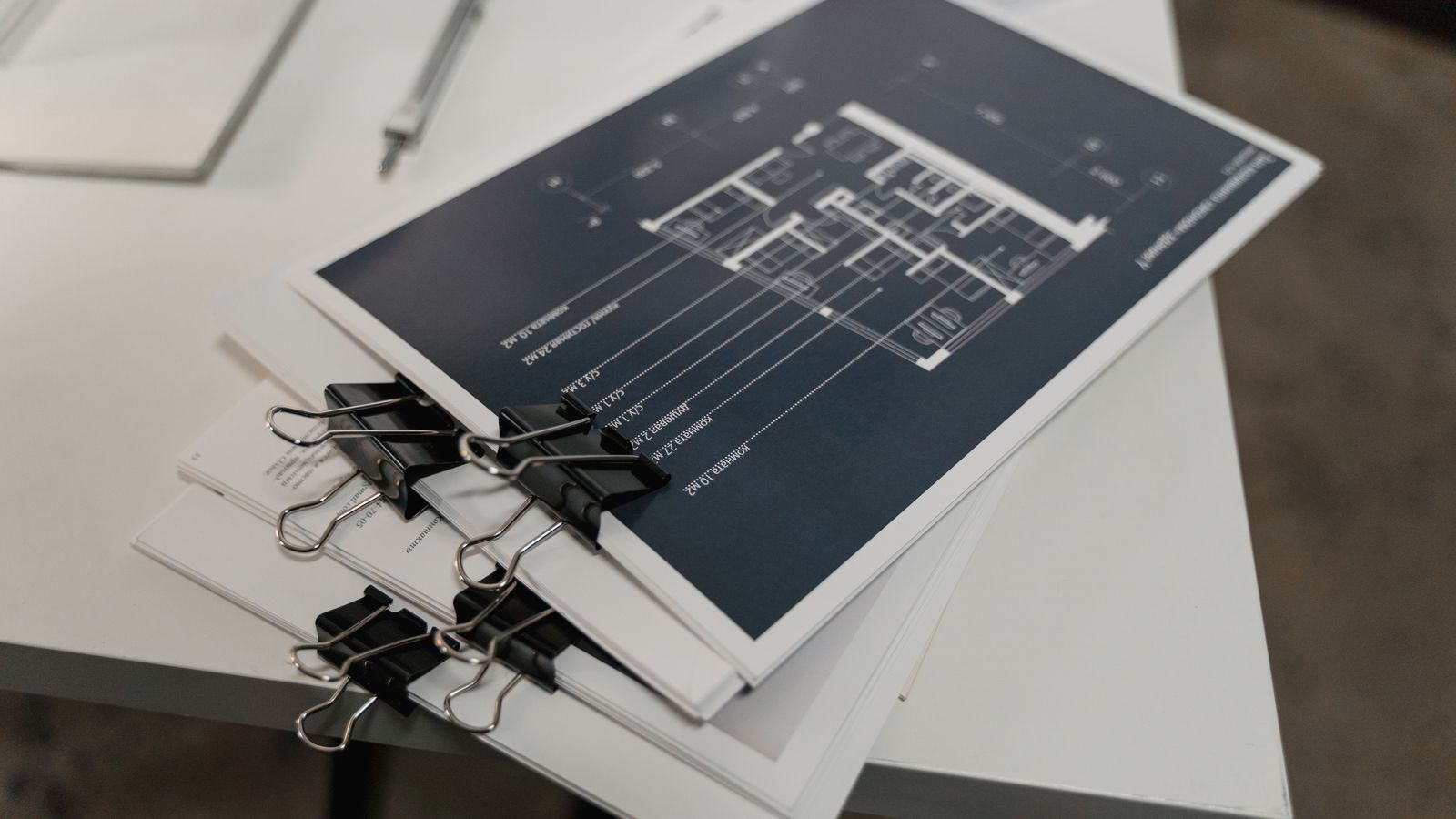 Piles de plans d'architecture retenus par des pinces noires sur une table blanche.