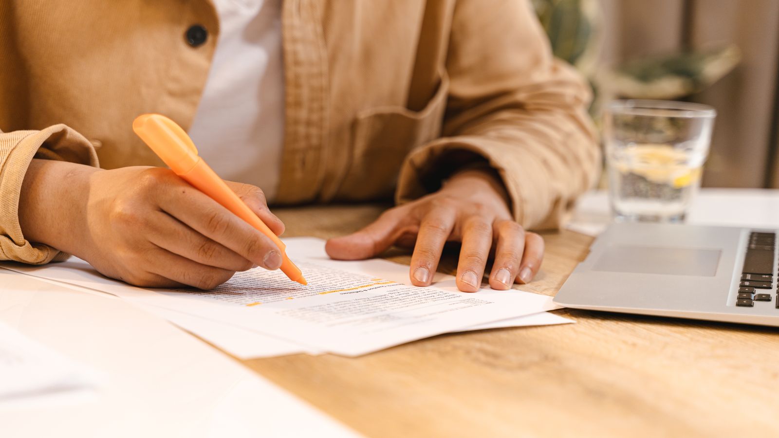 A person highlights a passage on printed pages next to a laptop