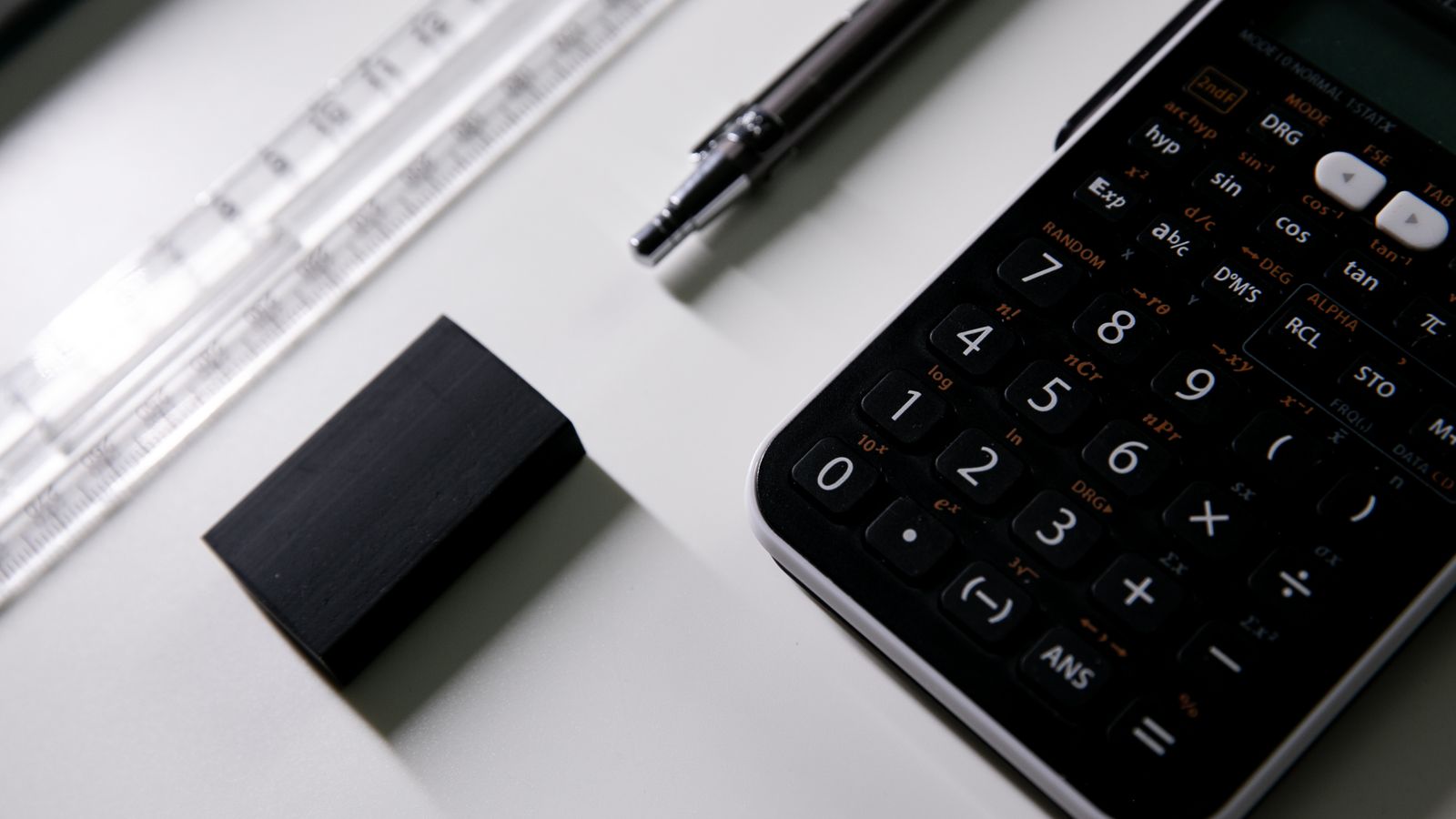 Scientific calculator, clear ruler and pen on a white desk, set up for exam preparation.