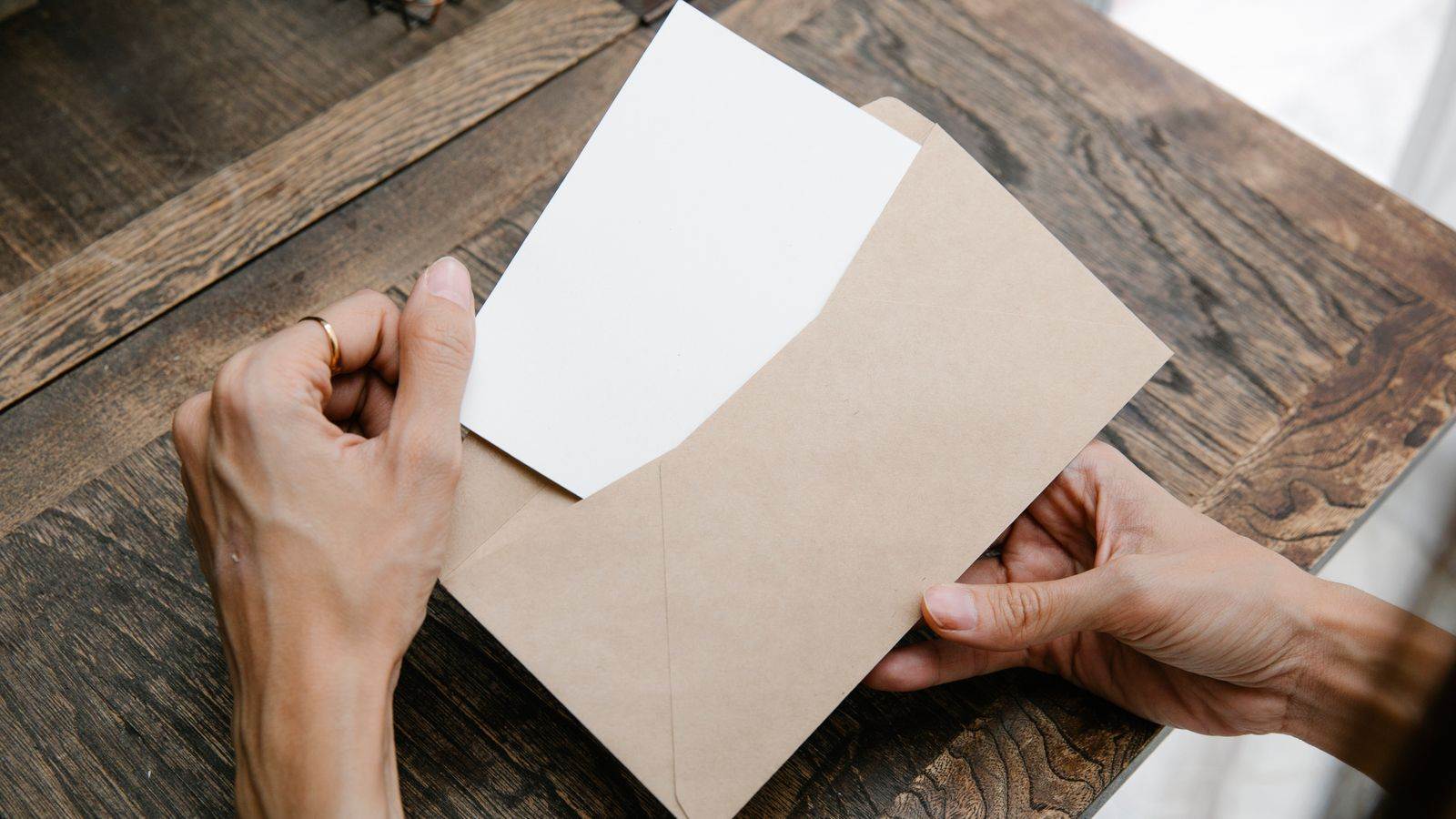 A person pulls a blank sheet out of a brown envelope on a wooden table.