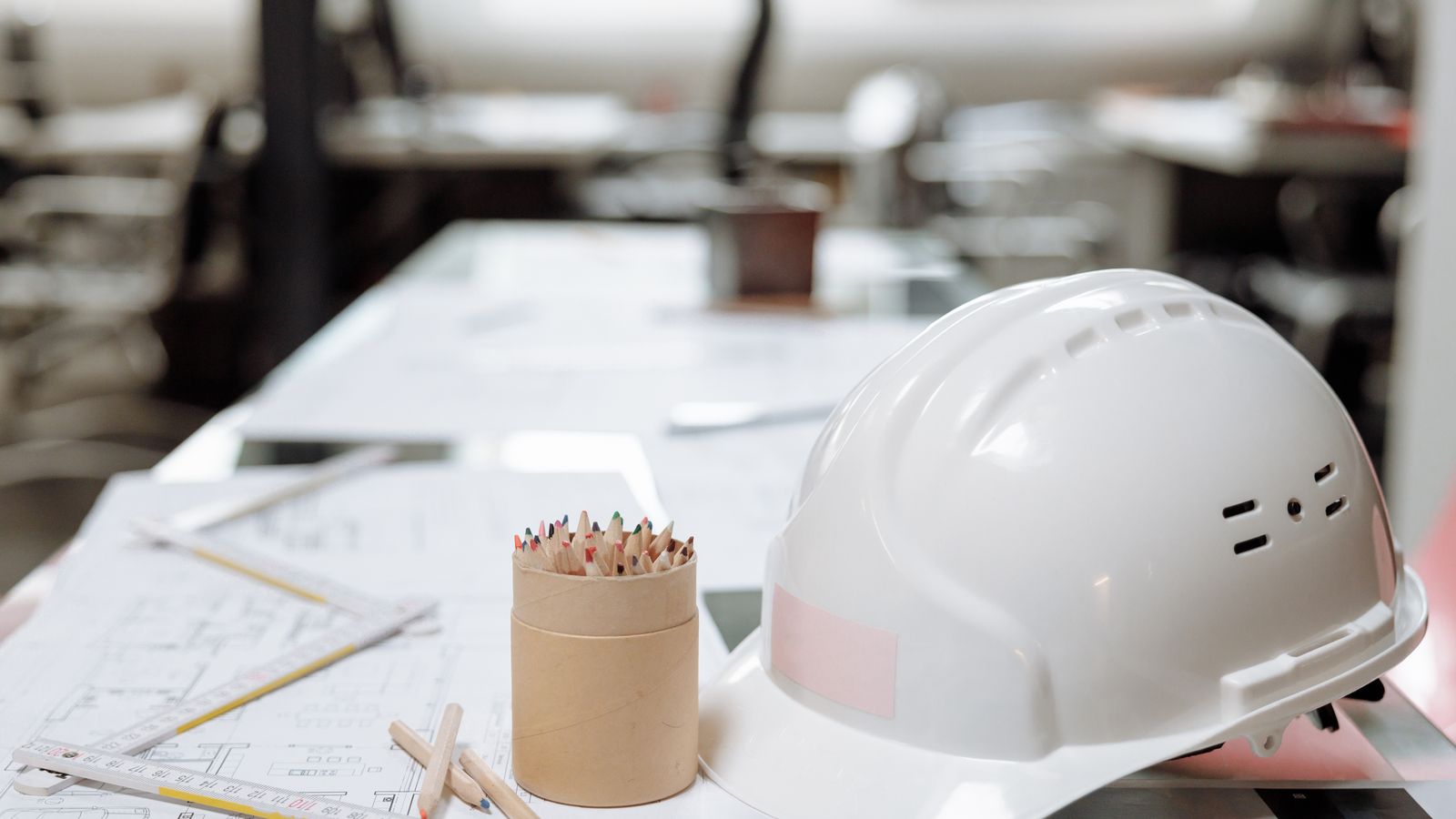 A white hard hat, coloured pencils and a folding ruler resting on building plans.