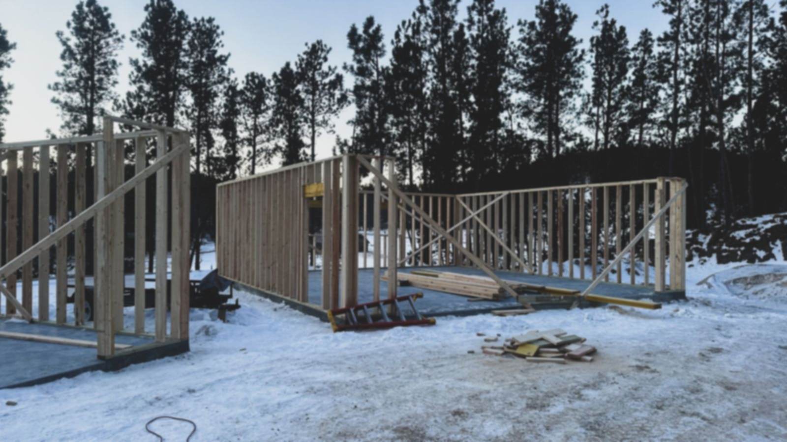 Charpente de bois d'un bâtiment en construction dans un boisé enneigé, en hiver.
