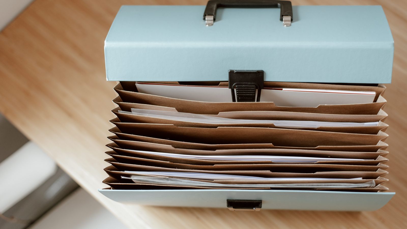 Un classeur à soufflet ouvert rempli de dossiers de documents, posé sur un bureau en bois