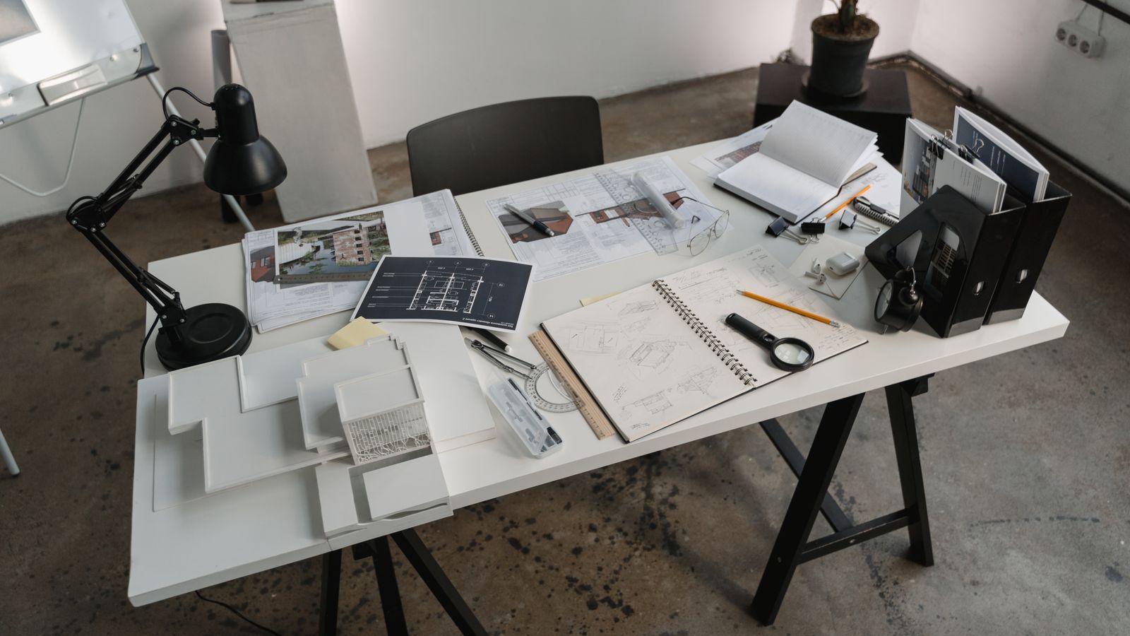 White desk covered with floor plans, sketches, a scale model and drafting tools.