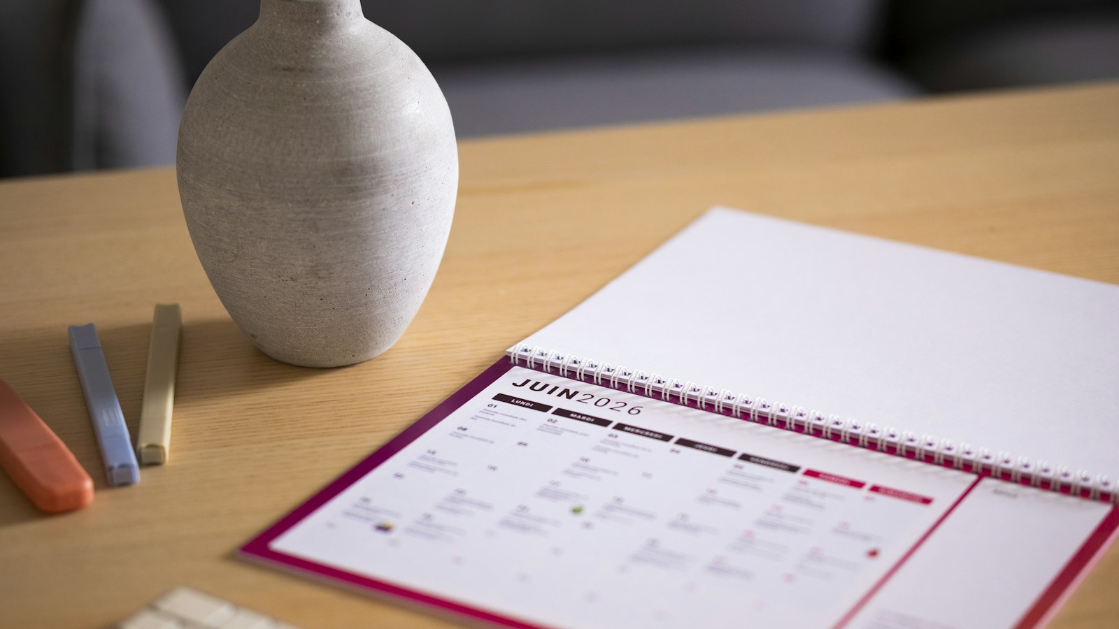 A desk calendar open to June on a wooden table beside a vase