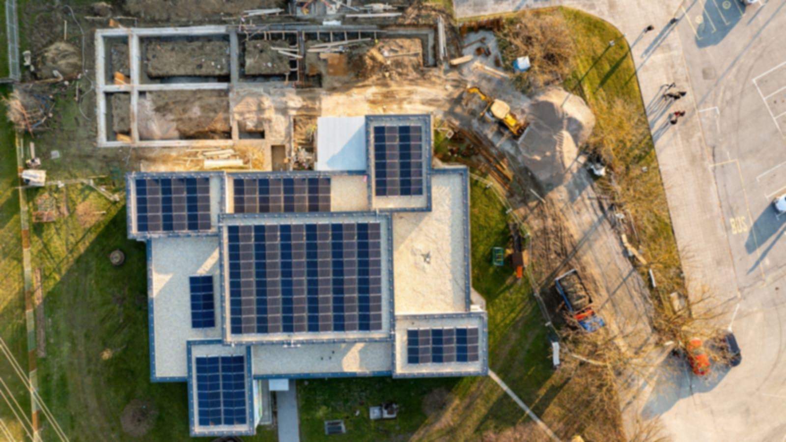 Aerial view of a building with rooftop solar panels beside a foundation excavation under construction