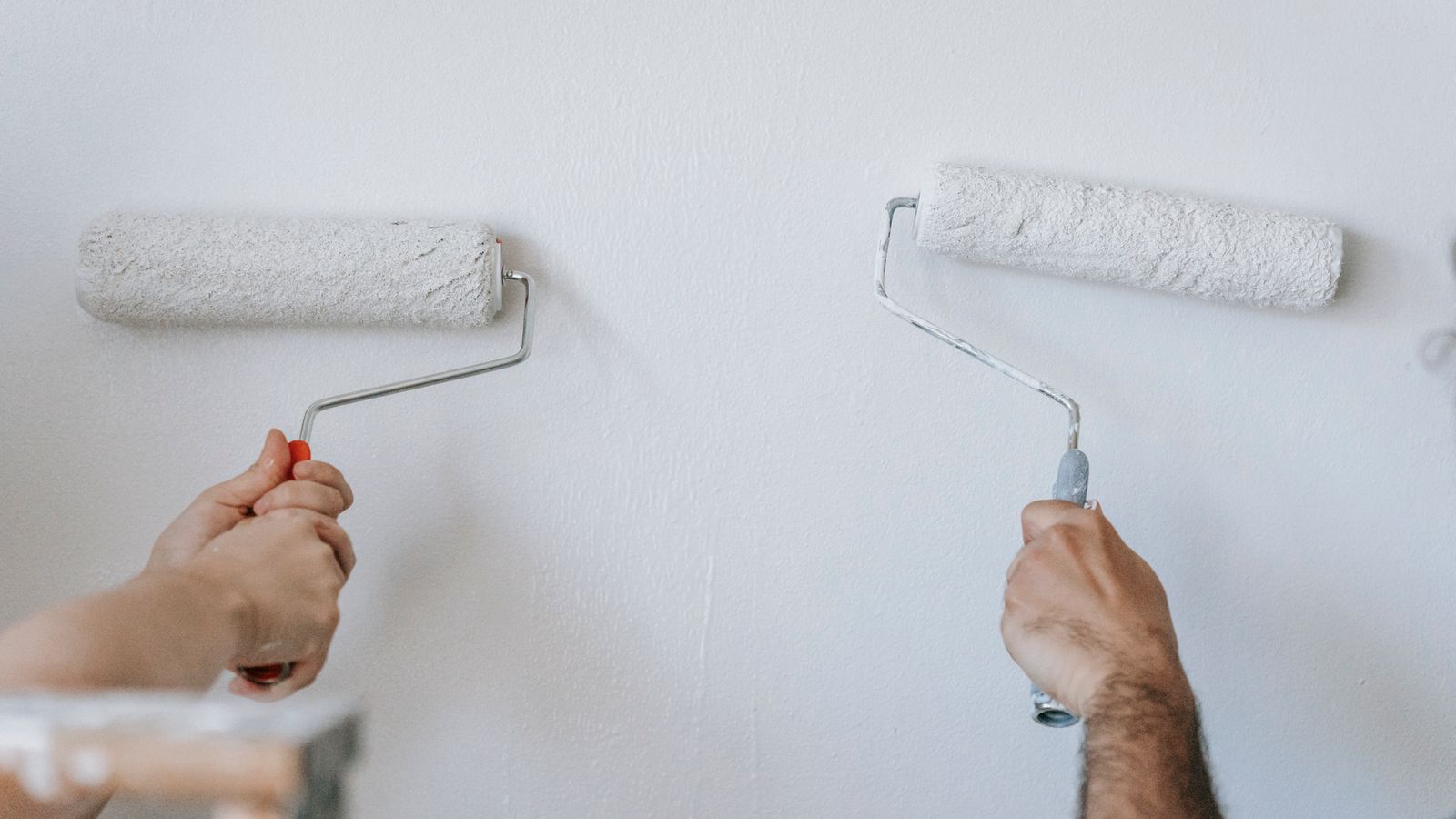 Deux personnes peignent un mur intérieur blanc au rouleau pendant des travaux de rénovation.